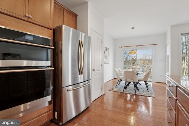 kitchen with appliances with stainless steel finishes, brown cabinetry, light wood-style floors, and hanging light fixtures