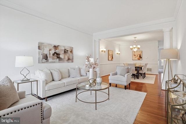 living room featuring wood finished floors, visible vents, ornamental molding, decorative columns, and an inviting chandelier