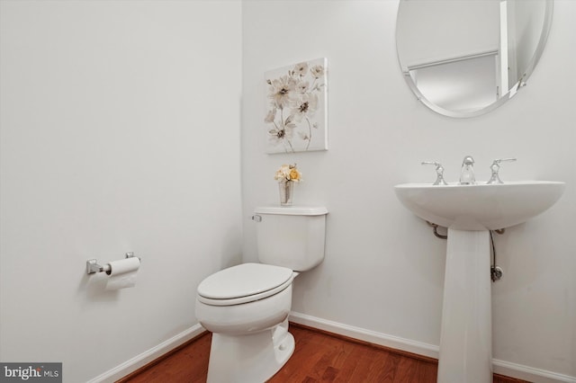 half bathroom with toilet, baseboards, and wood finished floors