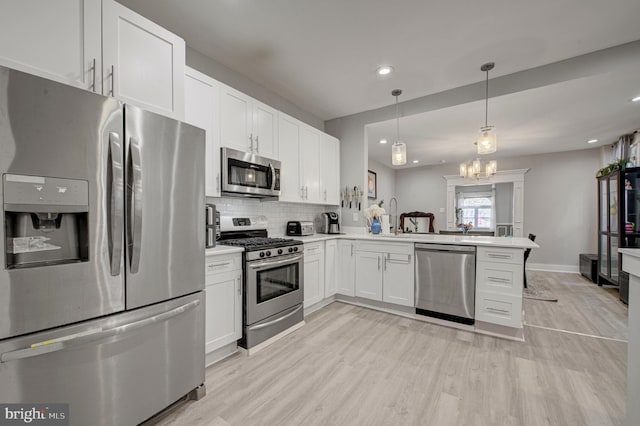 kitchen featuring a peninsula, light countertops, appliances with stainless steel finishes, decorative backsplash, and light wood finished floors