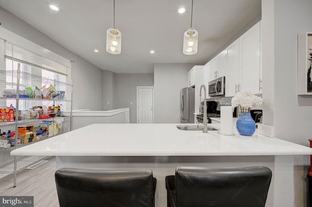 kitchen with stainless steel appliances, a peninsula, light wood-type flooring, decorative backsplash, and a kitchen bar