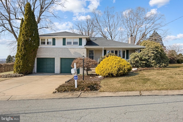 tri-level home with brick siding, a chimney, a garage, driveway, and a front lawn