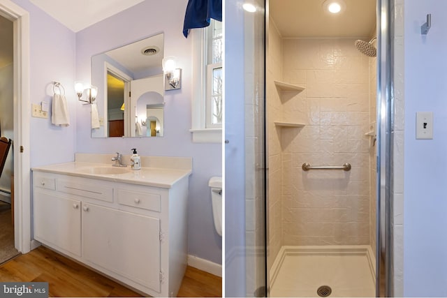 full bath with toilet, a stall shower, vanity, wood finished floors, and baseboards