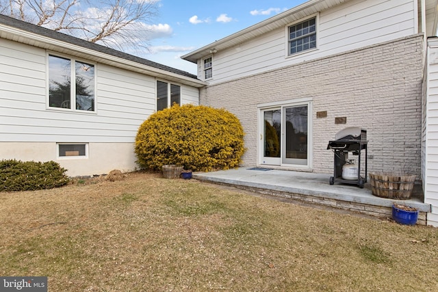 rear view of property with brick siding, a patio, and a lawn