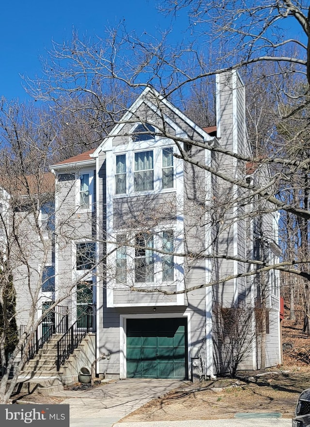 view of front facade with an attached garage, a chimney, and concrete driveway