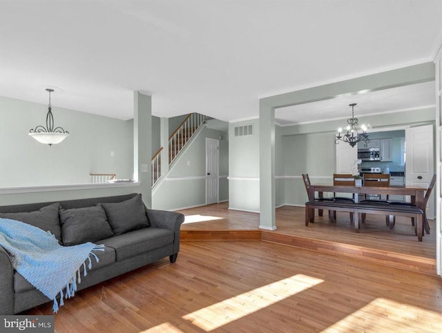 living area with visible vents, stairway, a chandelier, light wood-type flooring, and baseboards