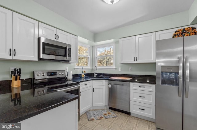 kitchen with dark stone countertops, appliances with stainless steel finishes, white cabinets, and a sink