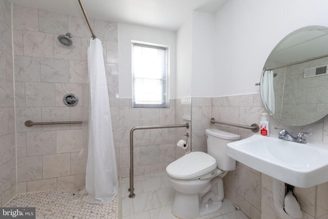 bathroom with toilet, a wainscoted wall, visible vents, tile walls, and a tile shower