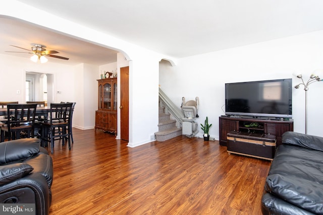 living area with arched walkways, ceiling fan, stairway, and wood finished floors