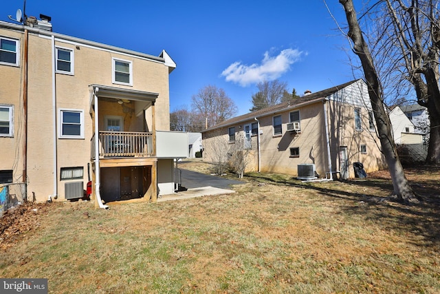 back of house with central AC, a lawn, and stucco siding