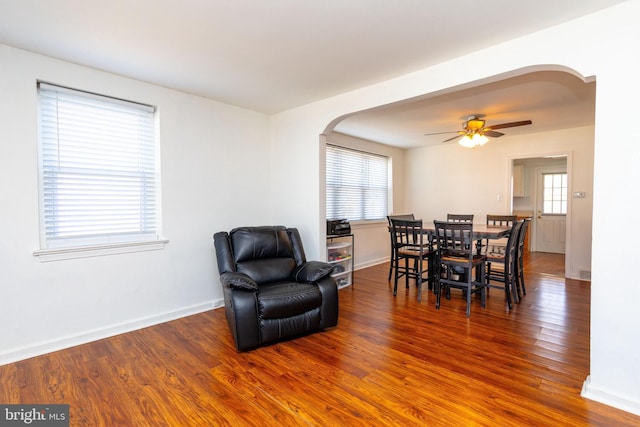 dining room featuring arched walkways, baseboards, and wood finished floors