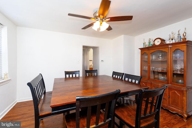 dining area featuring baseboards, ceiling fan, arched walkways, and dark wood-type flooring