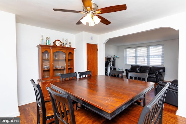 dining space with a ceiling fan, arched walkways, baseboards, and wood finished floors