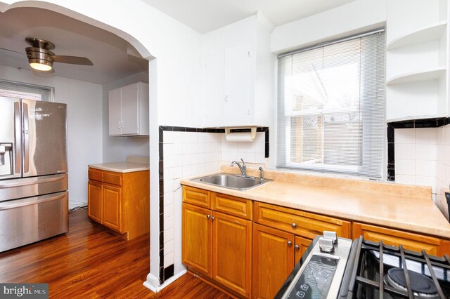 kitchen featuring dark wood-style floors, stove, a ceiling fan, a sink, and stainless steel fridge