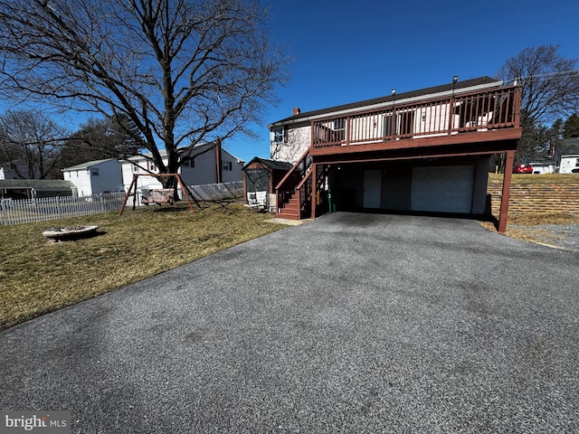 view of front of house with a front yard, fence, driveway, a wooden deck, and an attached garage