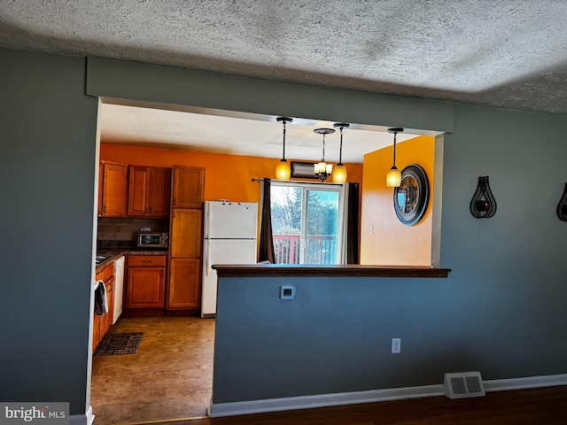 kitchen with baseboards, visible vents, freestanding refrigerator, decorative backsplash, and brown cabinets