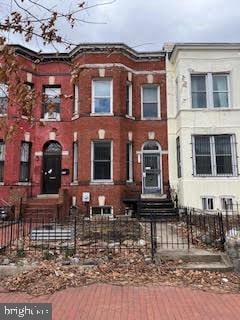 townhome / multi-family property featuring a fenced front yard and brick siding