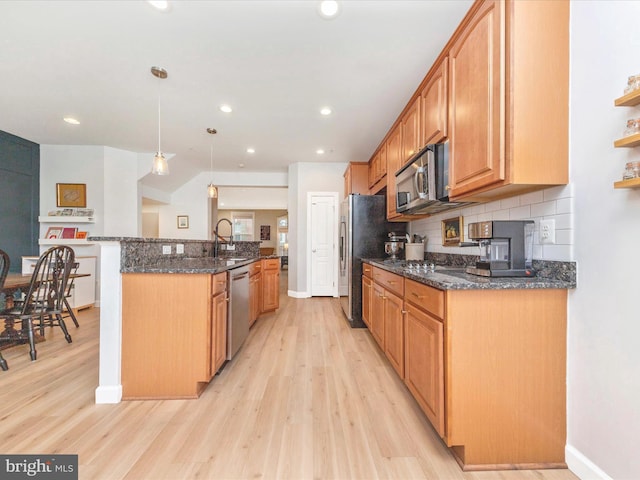 kitchen with stainless steel appliances, a sink, light wood-style flooring, and decorative backsplash