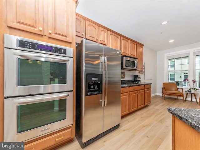 kitchen with stainless steel appliances, dark stone counters, light wood-style floors, and decorative backsplash