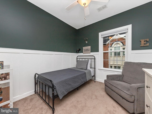 bedroom with wainscoting, carpet, visible vents, and a ceiling fan