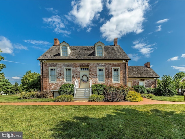 view of front facade featuring brick siding, a chimney, and a front yard