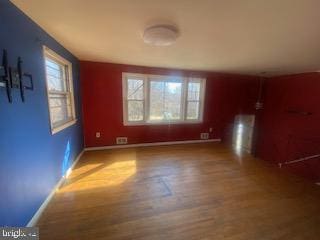 empty room featuring a healthy amount of sunlight, baseboards, and wood finished floors