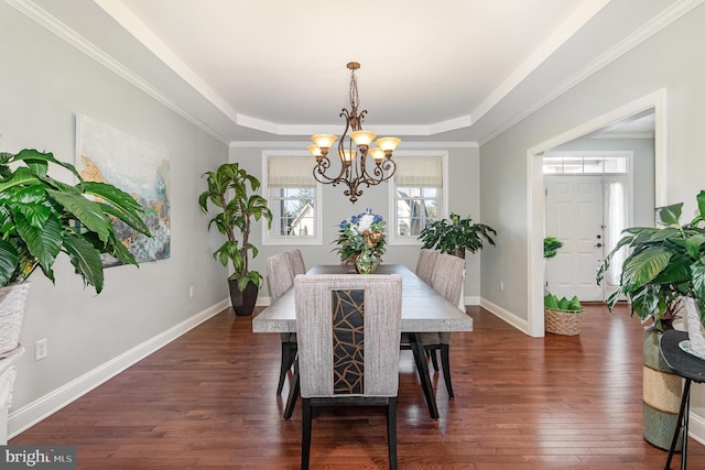 dining area featuring a raised ceiling, ornamental molding, dark wood-style floors, baseboards, and a chandelier