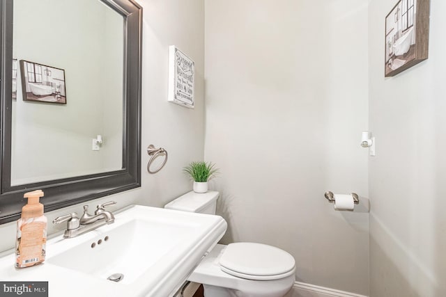 half bath featuring toilet, baseboards, and a sink