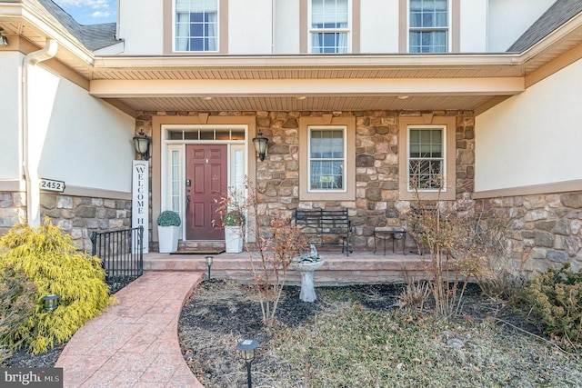 entrance to property featuring covered porch, stone siding, and stucco siding