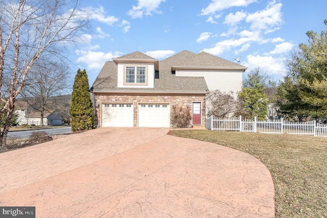 view of front facade featuring a shingled roof, fence, concrete driveway, a front yard, and stone siding