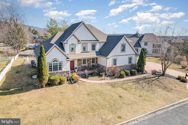 view of front facade featuring stucco siding, stone siding, a front yard, and fence