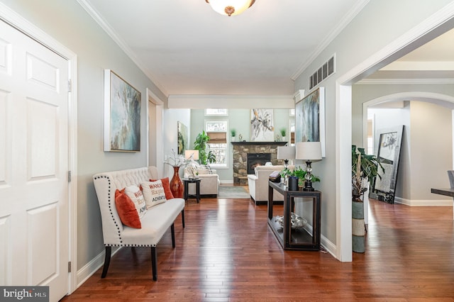 sitting room with visible vents, ornamental molding, a stone fireplace, and hardwood / wood-style flooring