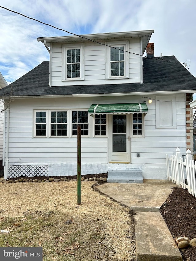 view of front of home with roof with shingles, a chimney, and fence