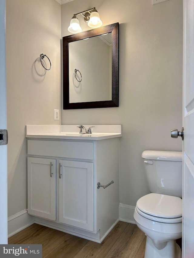 half bath featuring toilet, baseboards, wood finished floors, and vanity