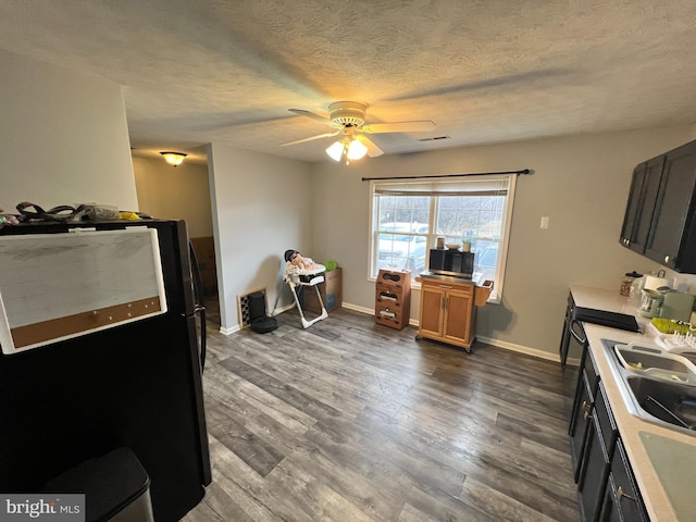 kitchen featuring dark wood-style flooring, light countertops, stainless steel microwave, freestanding refrigerator, and a textured ceiling