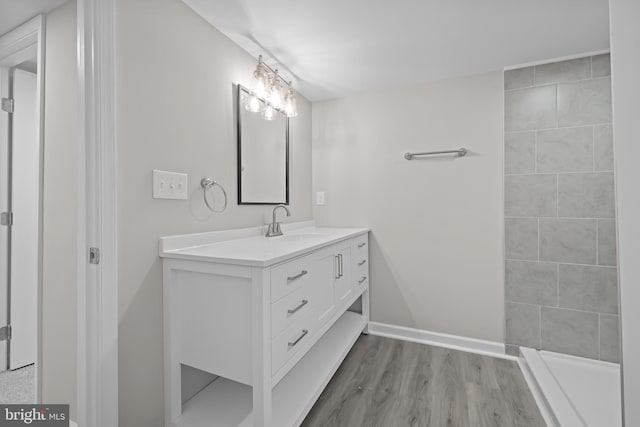 full bathroom featuring a tile shower, vanity, baseboards, and wood finished floors