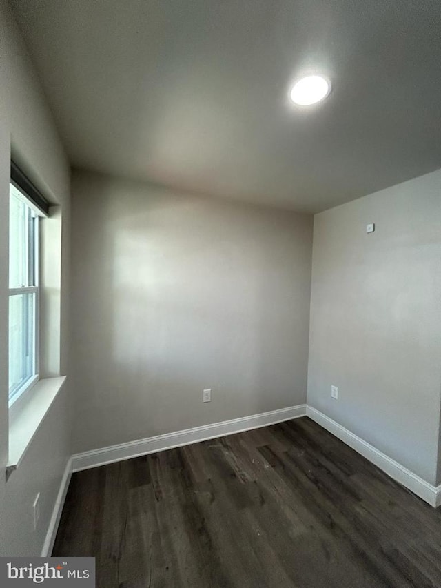 unfurnished room featuring baseboards and dark wood-style flooring