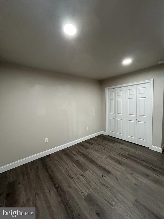 unfurnished bedroom with a closet, recessed lighting, dark wood-type flooring, and baseboards