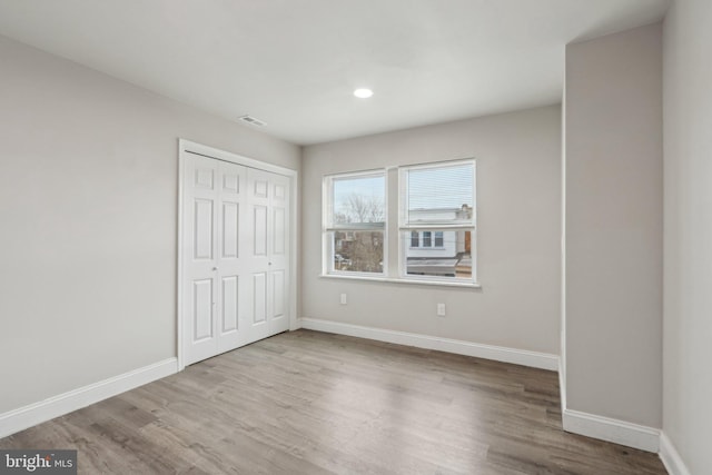 unfurnished bedroom featuring wood finished floors, baseboards, visible vents, recessed lighting, and a closet