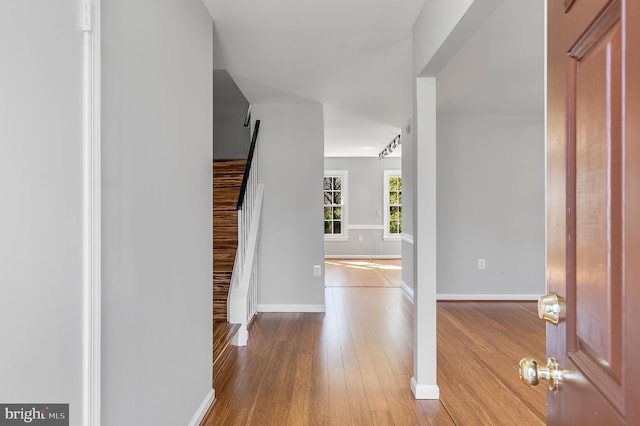 corridor featuring stairway, rail lighting, baseboards, and wood finished floors