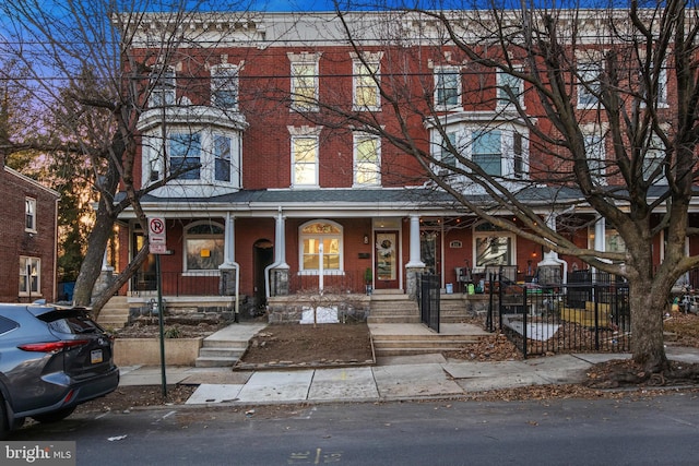 townhome / multi-family property featuring covered porch, brick siding, and fence