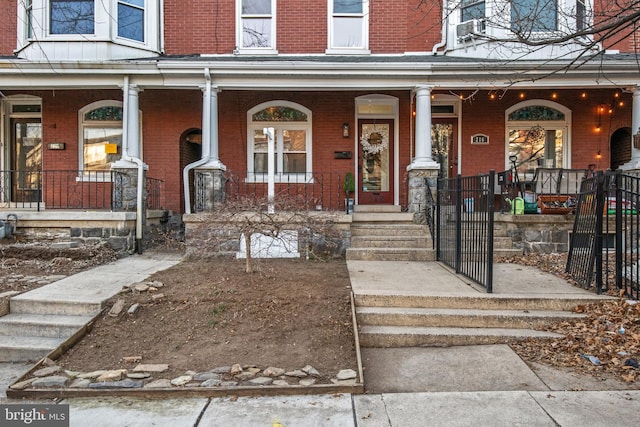 view of front of house with covered porch, fence, and brick siding