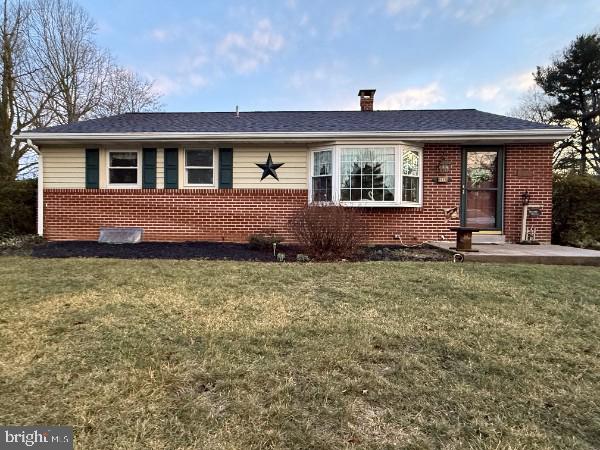 single story home featuring roof with shingles, brick siding, a front lawn, and a chimney