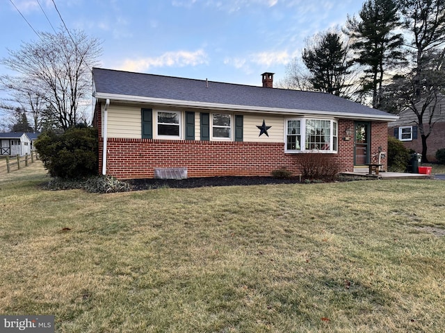 ranch-style home with roof with shingles, brick siding, a chimney, and a front yard