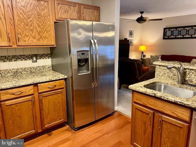 kitchen featuring light wood finished floors, a sink, decorative backsplash, stainless steel appliances, and open floor plan