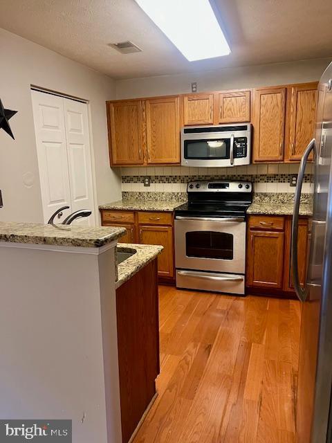 kitchen with brown cabinetry, light wood-style floors, tasteful backsplash, and appliances with stainless steel finishes