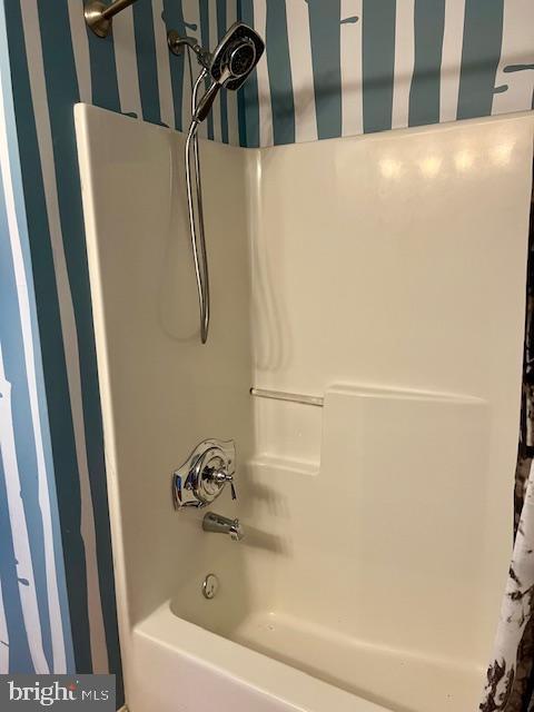 bathroom featuring wallpapered walls and shower / tub combo with curtain