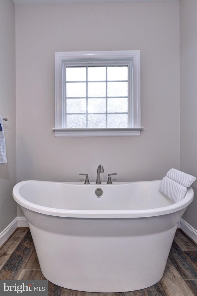 full bath with a freestanding tub, wood finished floors, and baseboards