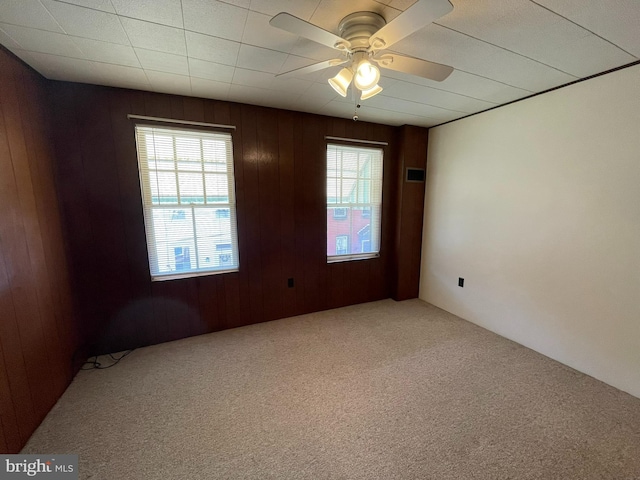 spare room featuring carpet flooring, ceiling fan, and wooden walls