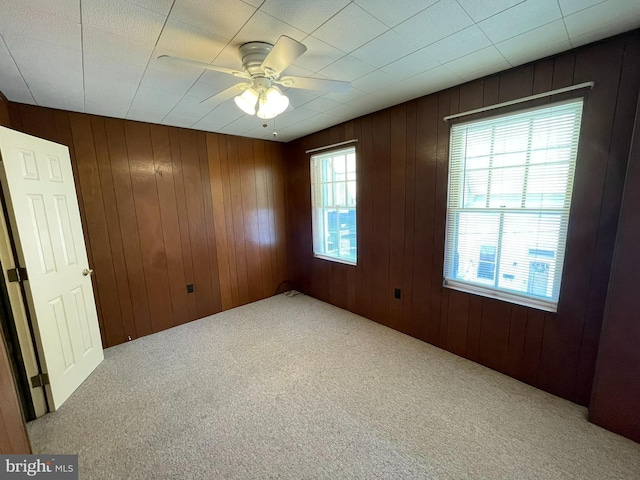 carpeted empty room featuring a healthy amount of sunlight, wooden walls, and a ceiling fan